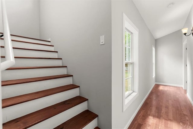 stairs with wood finished floors, baseboards, and vaulted ceiling