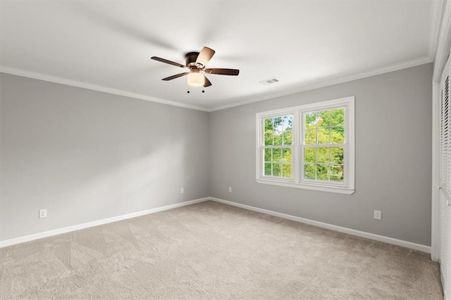 carpeted spare room with ceiling fan, visible vents, baseboards, and ornamental molding