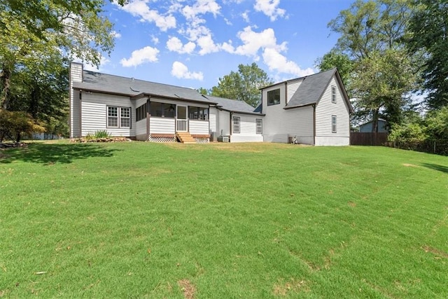 back of house with fence, a yard, roof with shingles, a sunroom, and a chimney