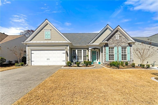 view of front of house featuring a shingled roof, a front lawn, a garage, stone siding, and aphalt driveway