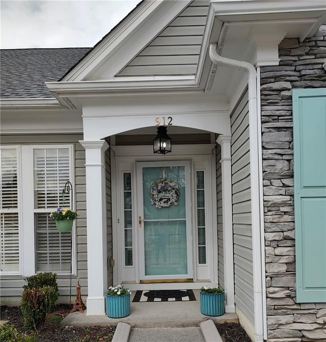 property entrance with stone siding, a porch, and a shingled roof