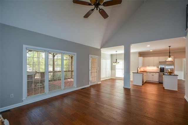 unfurnished living room featuring baseboards, dark wood-style flooring, a sink, ceiling fan with notable chandelier, and high vaulted ceiling