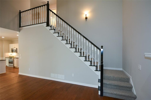 stairway with a towering ceiling, baseboards, visible vents, and wood finished floors