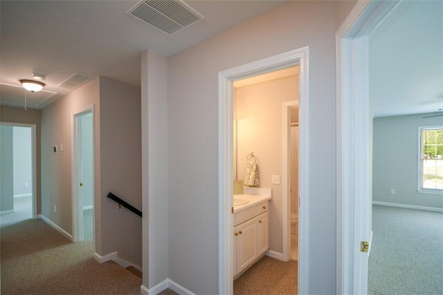 corridor with an upstairs landing, light colored carpet, attic access, and visible vents