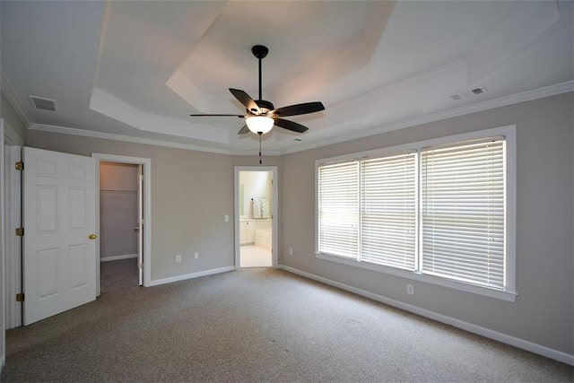 unfurnished bedroom with baseboards, carpet floors, a walk in closet, visible vents, and a tray ceiling