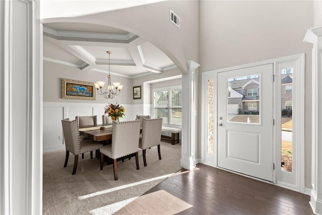 dining space with decorative columns, ornamental molding, coffered ceiling, dark wood-type flooring, and an inviting chandelier