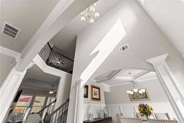 stairway with ornate columns, a towering ceiling, beamed ceiling, ornamental molding, and an inviting chandelier