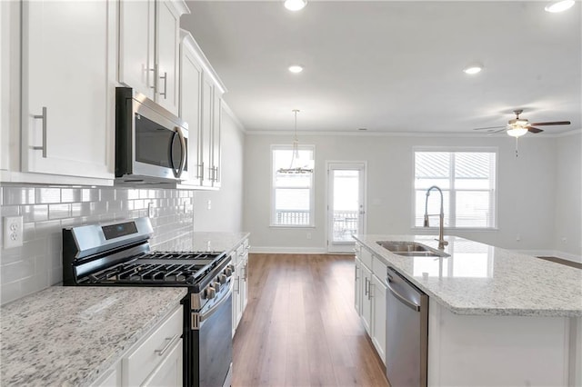 kitchen with a sink, white cabinets, appliances with stainless steel finishes, decorative backsplash, and crown molding