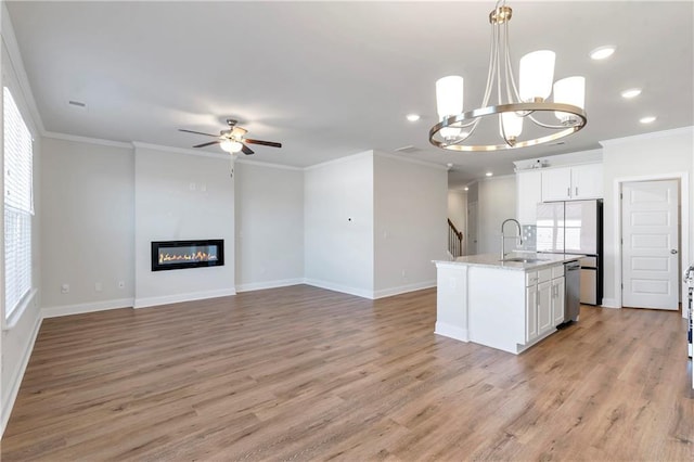 kitchen with a sink, ornamental molding, fridge, a glass covered fireplace, and a center island with sink