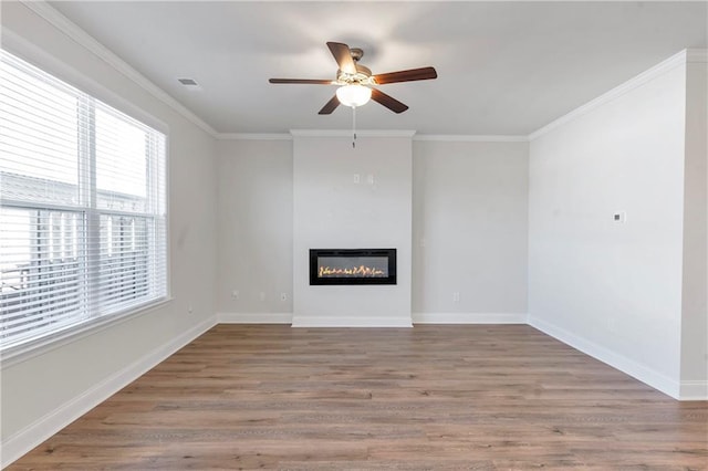 unfurnished living room featuring visible vents, ornamental molding, a glass covered fireplace, wood finished floors, and baseboards