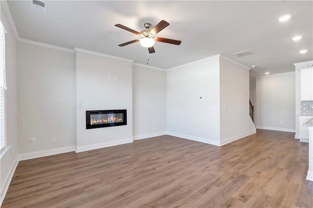 unfurnished living room with light wood-type flooring, a glass covered fireplace, ornamental molding, and baseboards