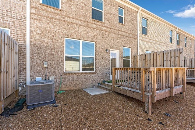 rear view of house with a deck, brick siding, fence, and central air condition unit