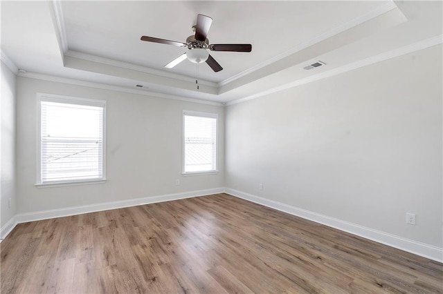 empty room featuring baseboards, visible vents, a raised ceiling, and wood finished floors