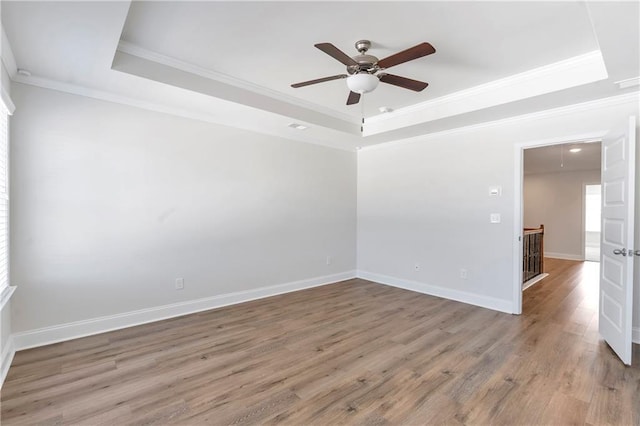 spare room with wood finished floors, a raised ceiling, attic access, and baseboards