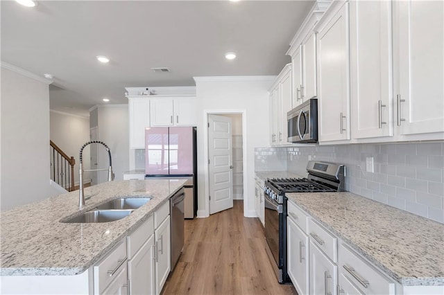 kitchen with decorative backsplash, appliances with stainless steel finishes, ornamental molding, light wood-type flooring, and a sink