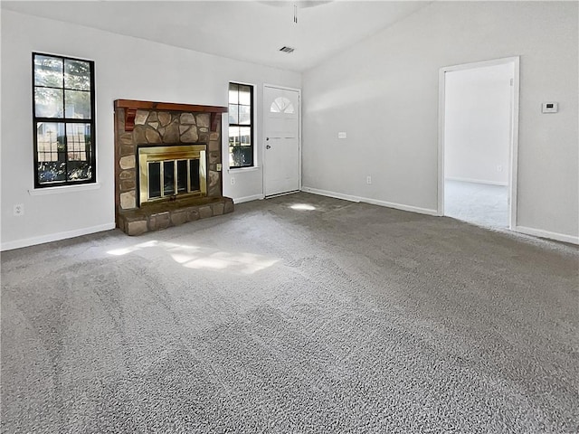 unfurnished living room with a wealth of natural light, a stone fireplace, and carpet