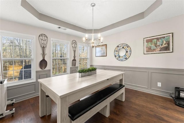 dining area featuring dark wood-type flooring, a raised ceiling, and a chandelier