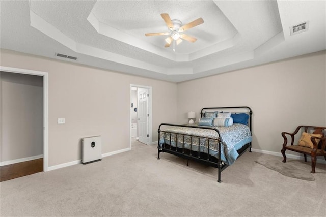 carpeted bedroom with ceiling fan, ensuite bath, a textured ceiling, and a tray ceiling