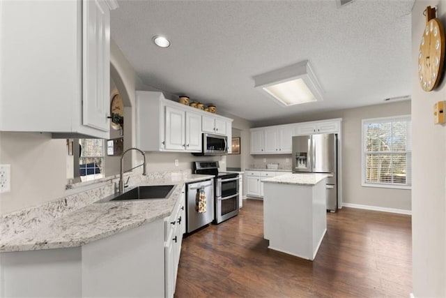 kitchen featuring sink, white cabinetry, a center island, appliances with stainless steel finishes, and light stone countertops