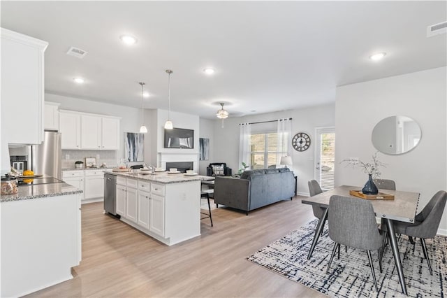 kitchen with stainless steel appliances, white cabinets, light hardwood / wood-style floors, and tasteful backsplash