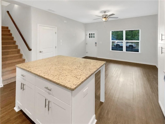 kitchen with ceiling fan, a kitchen island, light stone counters, dark hardwood / wood-style flooring, and white cabinets