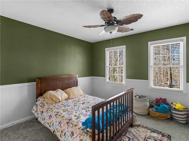 carpeted bedroom featuring a textured ceiling, ceiling fan, and multiple windows