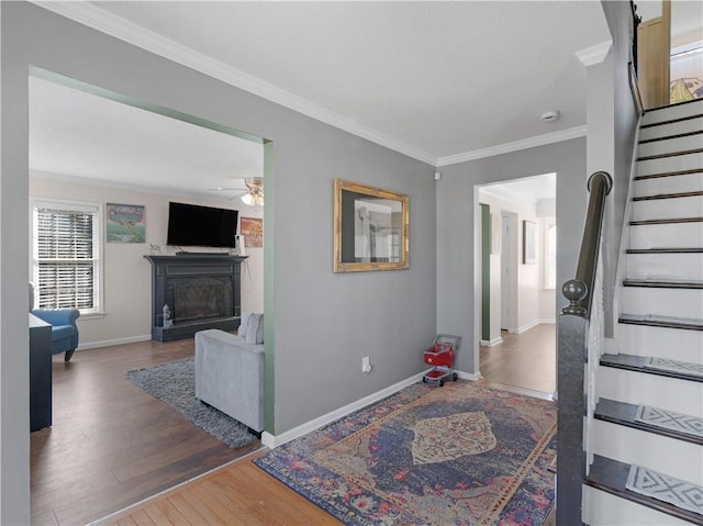 interior space with a fireplace, wood finished floors, baseboards, stairs, and crown molding