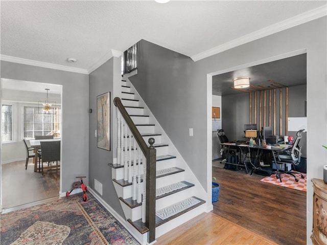 staircase with a textured ceiling, ornamental molding, wood finished floors, and an inviting chandelier