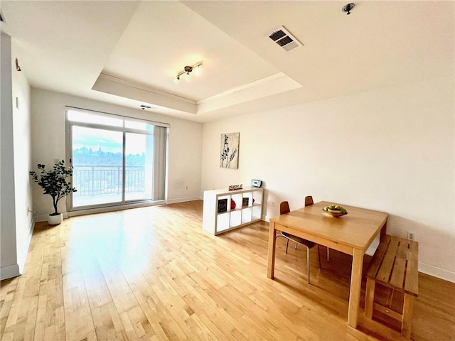 dining space featuring visible vents, light wood-style flooring, a raised ceiling, and baseboards