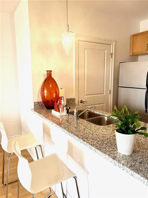 kitchen featuring a sink, light stone counters, light wood finished floors, and freestanding refrigerator