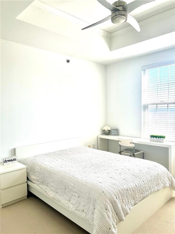 carpeted bedroom with a raised ceiling and a ceiling fan