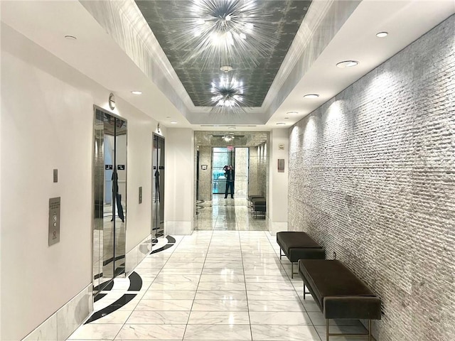 corridor featuring an accent wall, baseboards, a tray ceiling, elevator, and marble finish floor