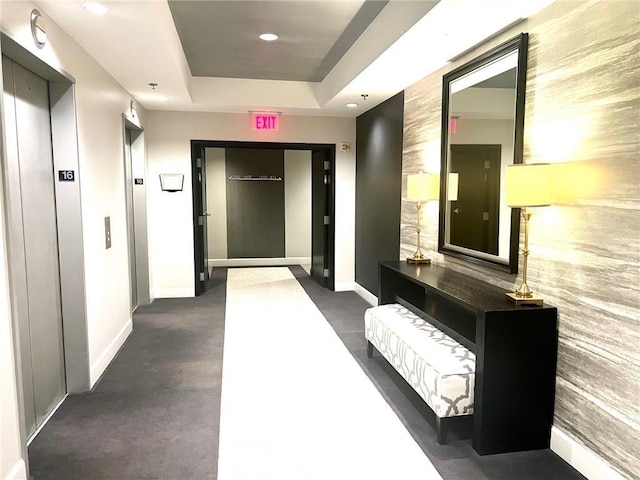 hallway with elevator, recessed lighting, baseboards, and a tray ceiling