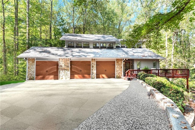 mid-century modern home with stone siding, driveway, a wooden deck, and an attached garage