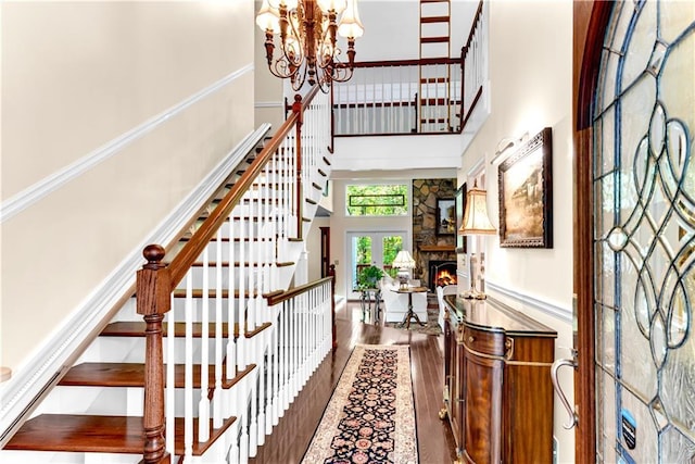 interior space featuring a fireplace, a high ceiling, an inviting chandelier, wood finished floors, and stairs