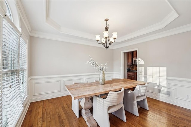 dining space with a healthy amount of sunlight, a raised ceiling, dark wood-type flooring, and an inviting chandelier