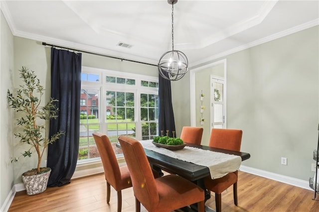 dining area featuring a chandelier, light wood-style flooring, ornamental molding, a raised ceiling, and baseboards