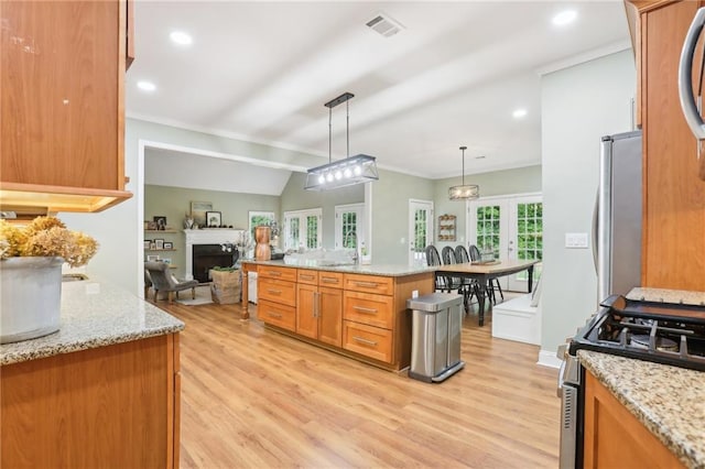 kitchen featuring stainless steel appliances, light wood-style flooring, open floor plan, a fireplace, and decorative light fixtures