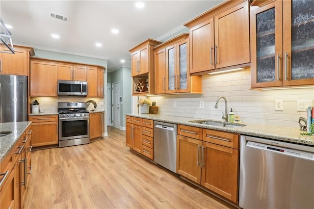 kitchen featuring appliances with stainless steel finishes, a sink, light wood finished floors, decorative backsplash, and light stone countertops