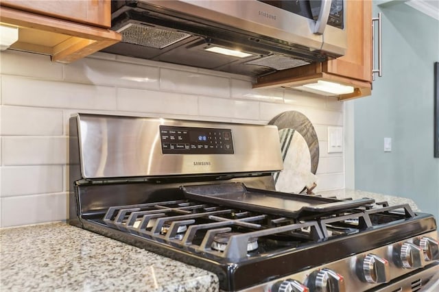 kitchen view of appliances with stainless steel finishes, decorative backsplash, and light stone counters