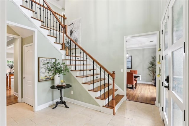 tiled foyer featuring a towering ceiling, stairway, and baseboards