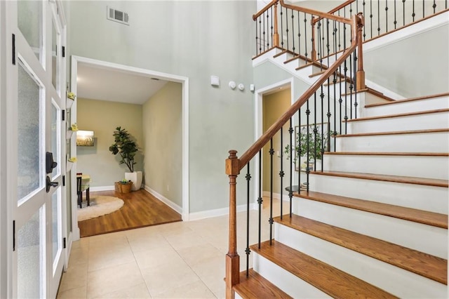 staircase featuring a towering ceiling, baseboards, french doors, and tile patterned flooring