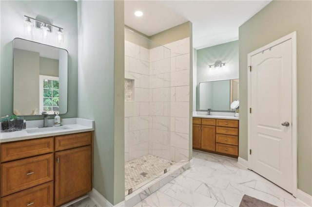 bathroom featuring marble look tiles, a walk in shower, two vanities, and baseboards