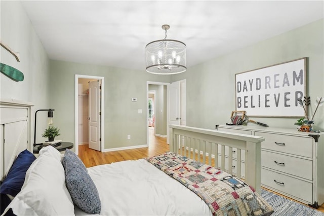 bedroom featuring a chandelier, light wood-type flooring, baseboards, and a walk in closet