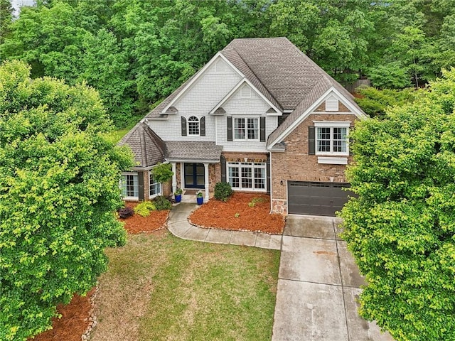 view of front facade with driveway, an attached garage, brick siding, a shingled roof, and a front lawn