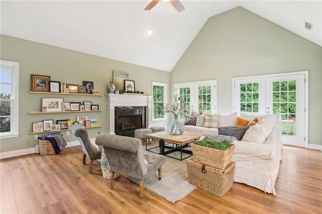 living room with french doors, high vaulted ceiling, ceiling fan, a premium fireplace, and wood finished floors