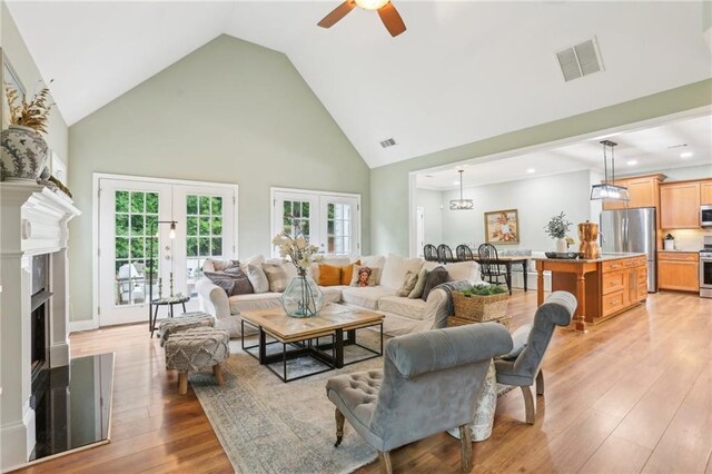 living area featuring high vaulted ceiling, ceiling fan, light wood-style flooring, recessed lighting, and a fireplace with raised hearth