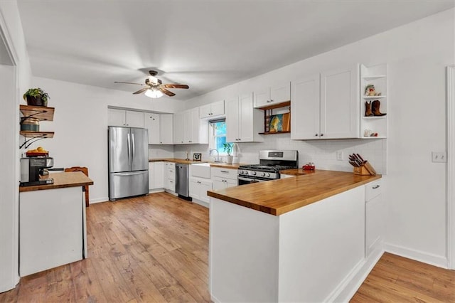 kitchen featuring stainless steel appliances, open shelves, a peninsula, a sink, and a ceiling fan