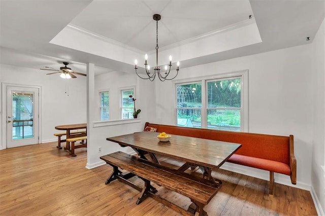 dining area featuring a tray ceiling, light wood finished floors, baseboards, and ornamental molding