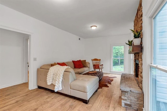 living area featuring light wood-type flooring, a stone fireplace, and baseboards